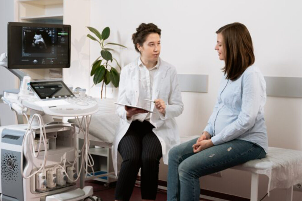A doctor sitting with a female patient on a bed going over results. there is a machine to the left of them.
